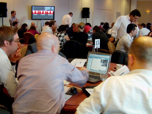 Simulation event with teams at numbered tables and countdown timer on LCD screen