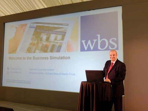 Facilitator on stage for WBS business simulation standing in front of projector screen