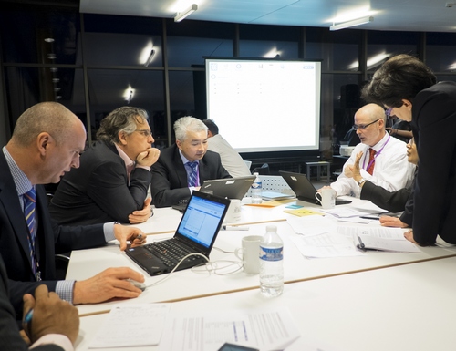 Team members around table during a leadership workshop discussing sim and studying results on laptop